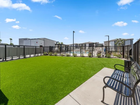 Fenced dog park with green turf and a bench