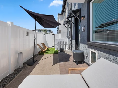 Fenced side patio with lounge seating and a shade sail