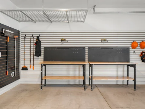 Garage workbenches and wall-mounted tools beneath an overhead storage rack