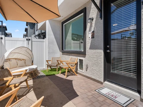 Private fenced patio with wood chairs, a hanging chair, and an umbrella