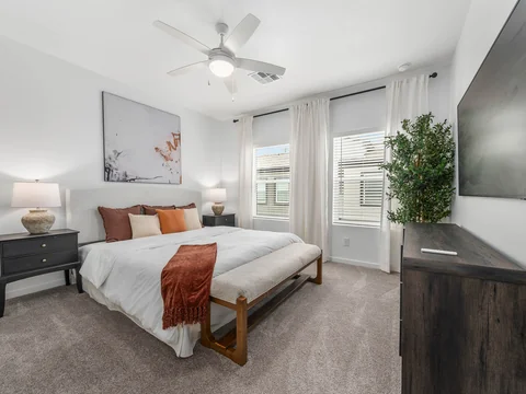 Bright bedroom with a white duvet, rust-colored throw, and large windows