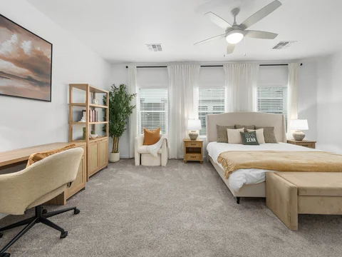 Wide bedroom view with a desk, bed, and reading chair by the windows
